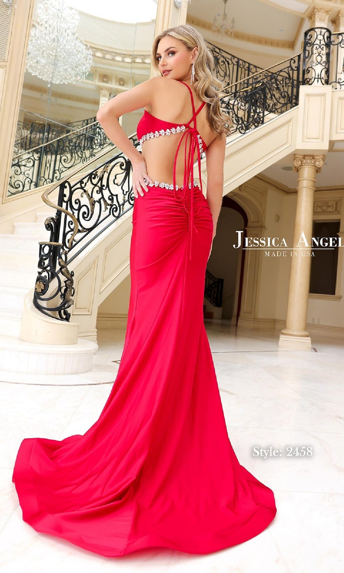 A woman poses on ornate stairs wearing the Jessica Angel 2458 Cut-Out Long Halter Prom Dress in bright red, a floor-length gown with elegant cutout details.